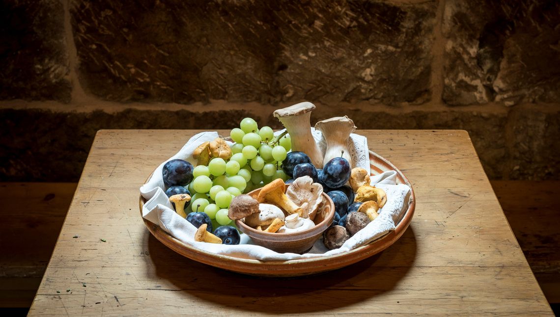 Detailaufnahme von Trauben, Pflaumen und Pilzen in einer Holzschale